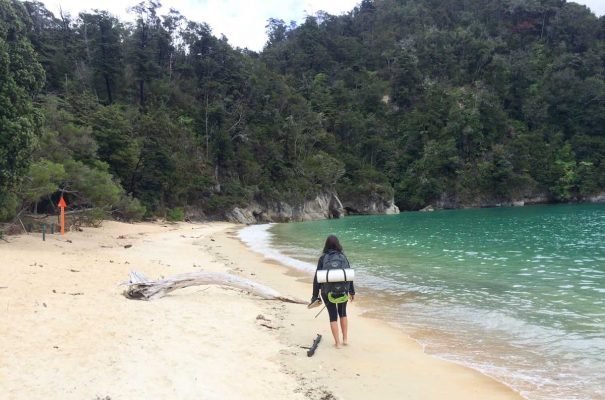 Mulher com mochila caminha em praia da costa de Abel Tasman