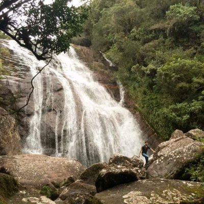 Homem caminha em pedras na frente da cachoeira dos Perdidos, perto de Curitiba