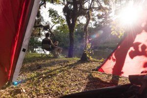 Homem na beira de um rio, visto de dentro de uma barraca de camping