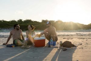 Amigos bebem e dão risada sentados na areia de uma praia