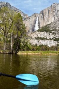 Remo-Rio-Merced-Yosemite Foto mostra o detalhe de um remo tocando as águas do rio Merced, com cachoeira ao fundo